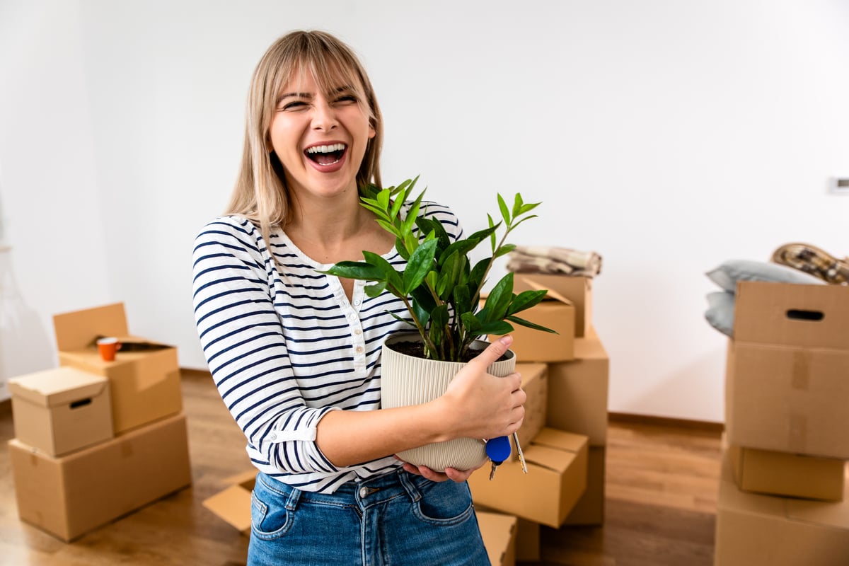A woman smiling holding a plant and house keys in front of boxes