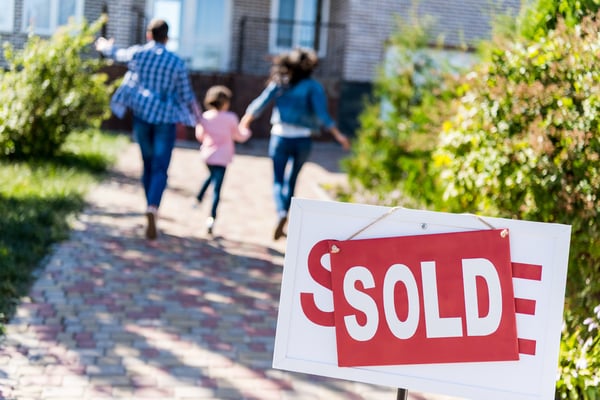 man woman and child running to a house in the background, for sale sign with sold over it in the foreground.