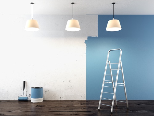 Room being painted blue with a ladder, paint bucket, and paint roller.