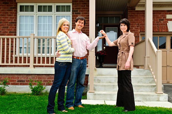 Woman handing keys to a couple standing in front of a house