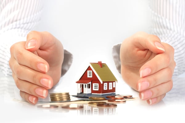 A model house with money around it covered by two hands