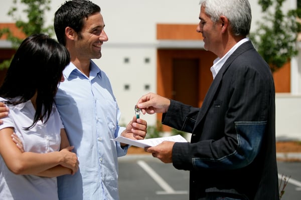 A man holding paperwork and keys is standing next to a man and a woman