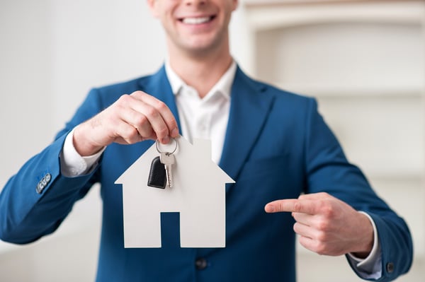 Man holding keys and a house model and pointing to them.