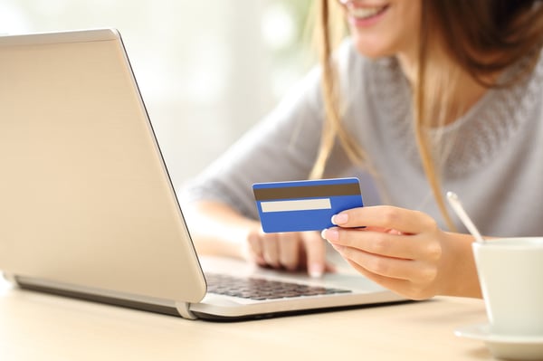 A woman holding a credit card making a payment on a laptop