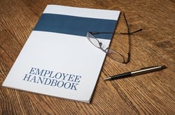 Employee handbook with glasses and a pen on a wooden table