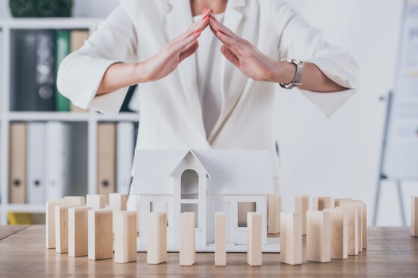 Partial view of risk manager covering house model surrounded with wooden blocks with hands
