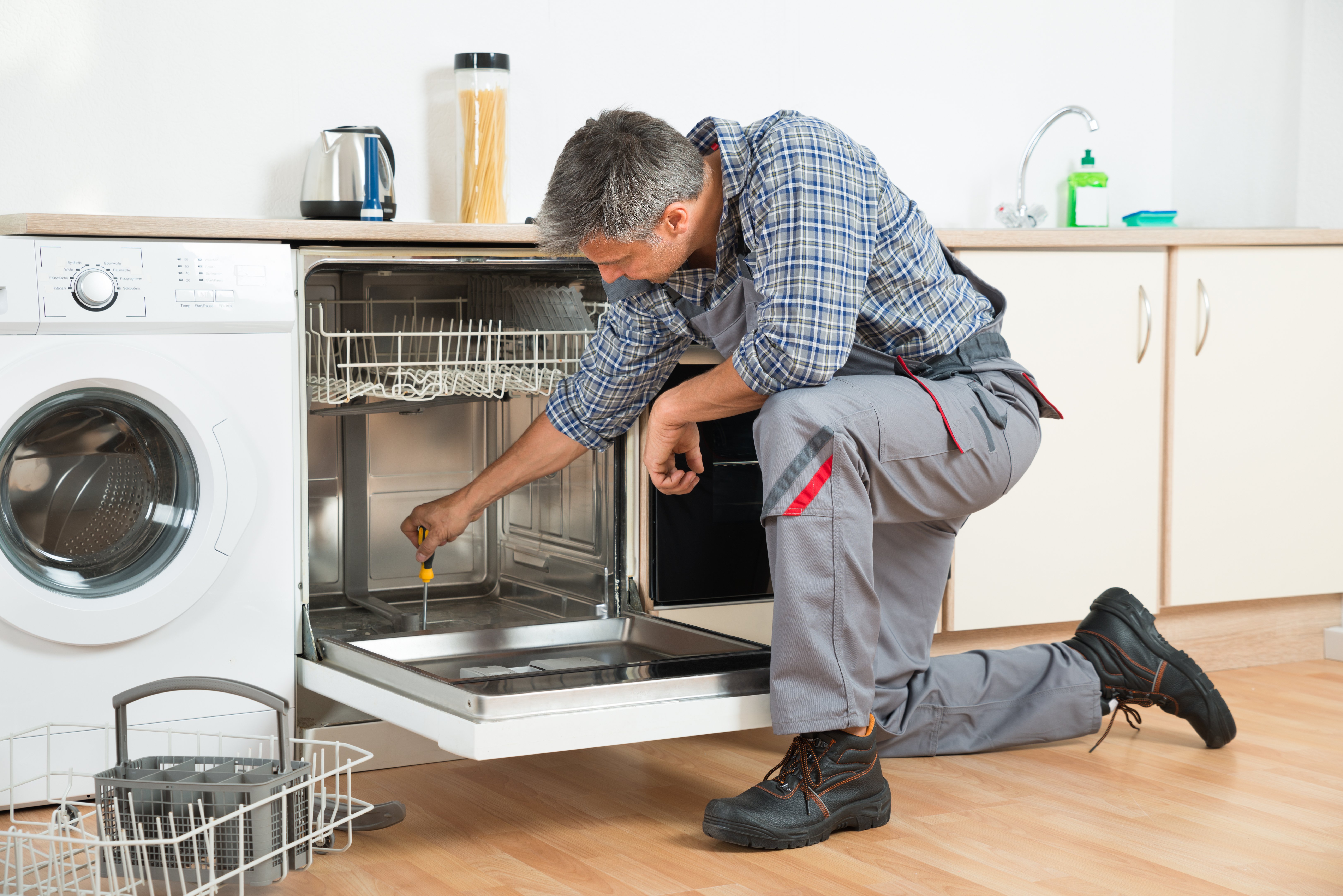 Repairman Repairing Dishwasher With Screwdriver In Kitchen