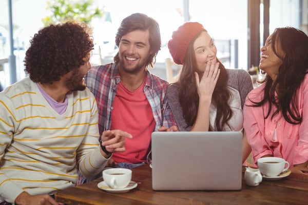 Laughing friends enjoying coffee with laptop in cafe