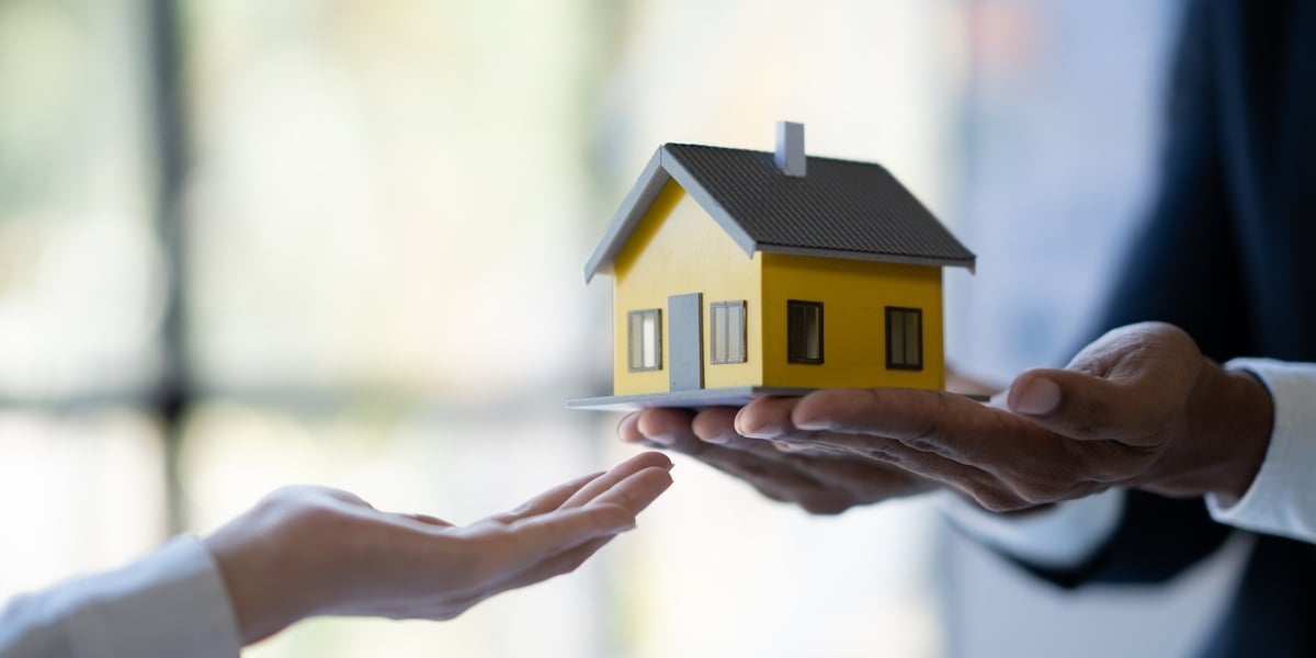 A person holding a model house and handing it to someone