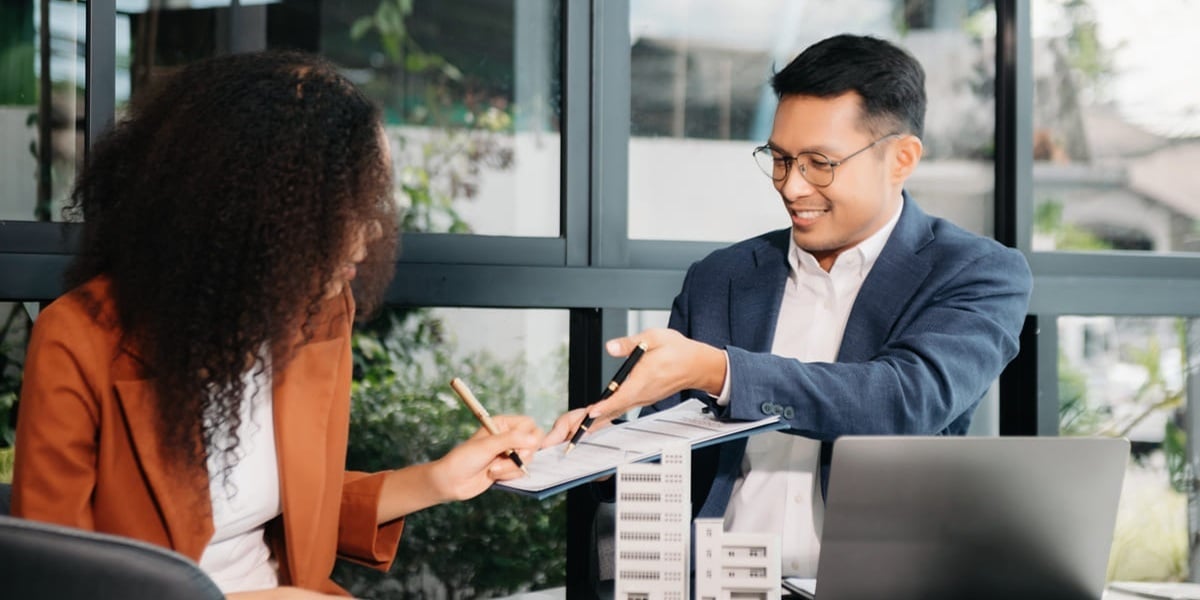 A woman signing a contract next to small commercial building models