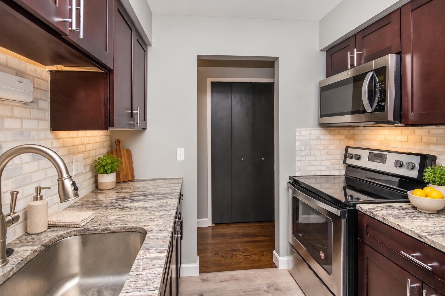 Galley kitchen with cherry shaker cabinets, granite counters, marble subway backsplash and stainless steel appliances