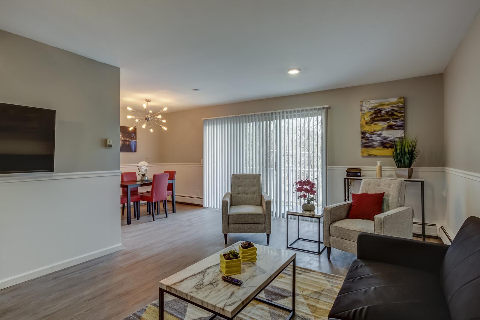 Living room with plank flooring, chair rail, two gray armchairs and a doorwall to a private balcony, with the dining area beyond