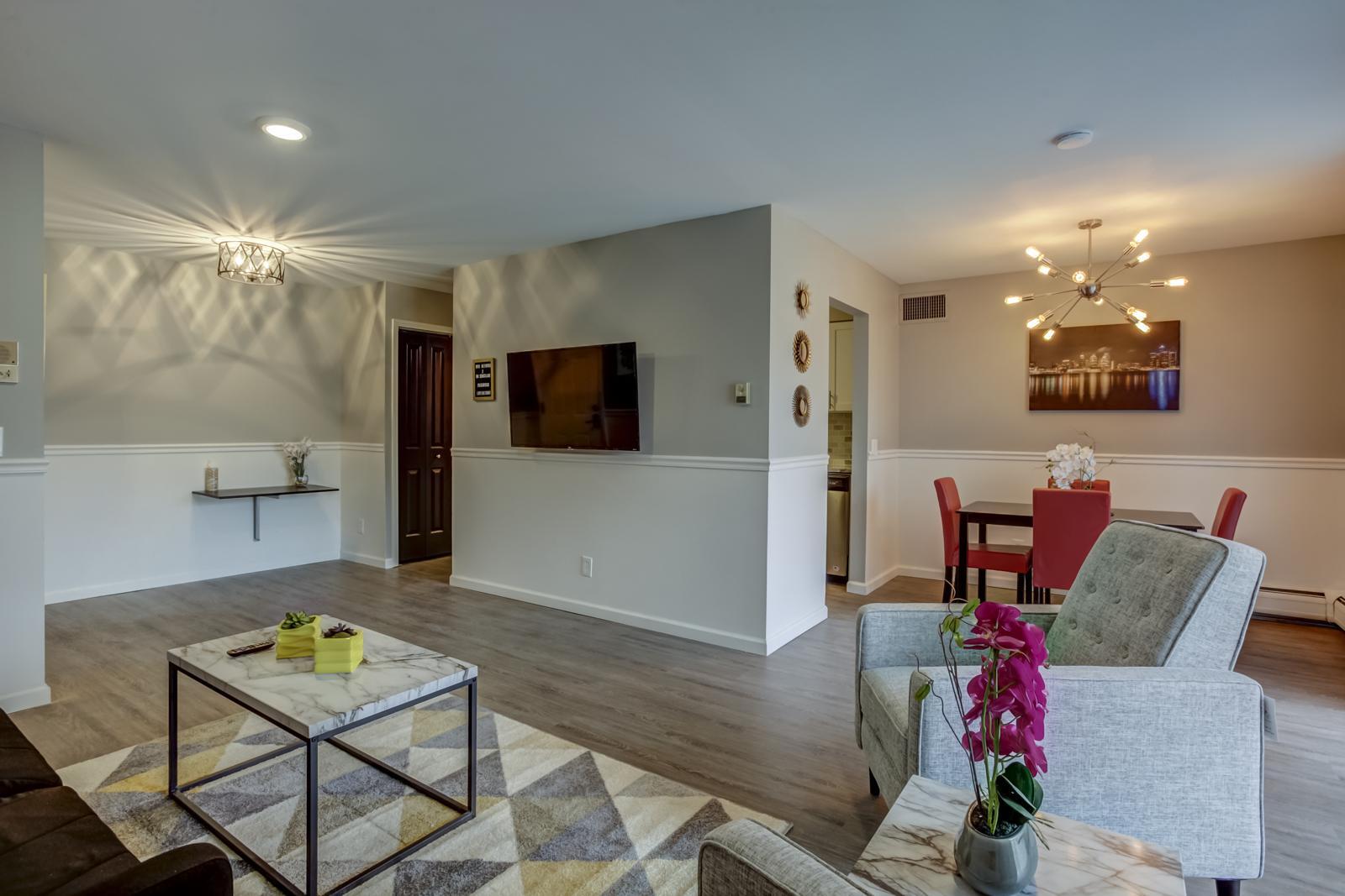 Open living and dining area with plank flooring, chair rail, wall-mounted TV and a starburst chandelier over the dining table