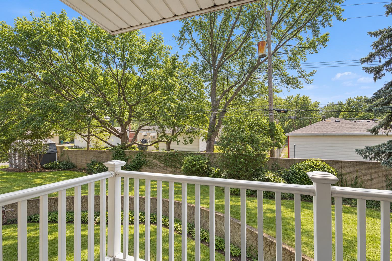 View from a private deck with white railing over a landscaped lawn, curved stone retaining wall and mature trees