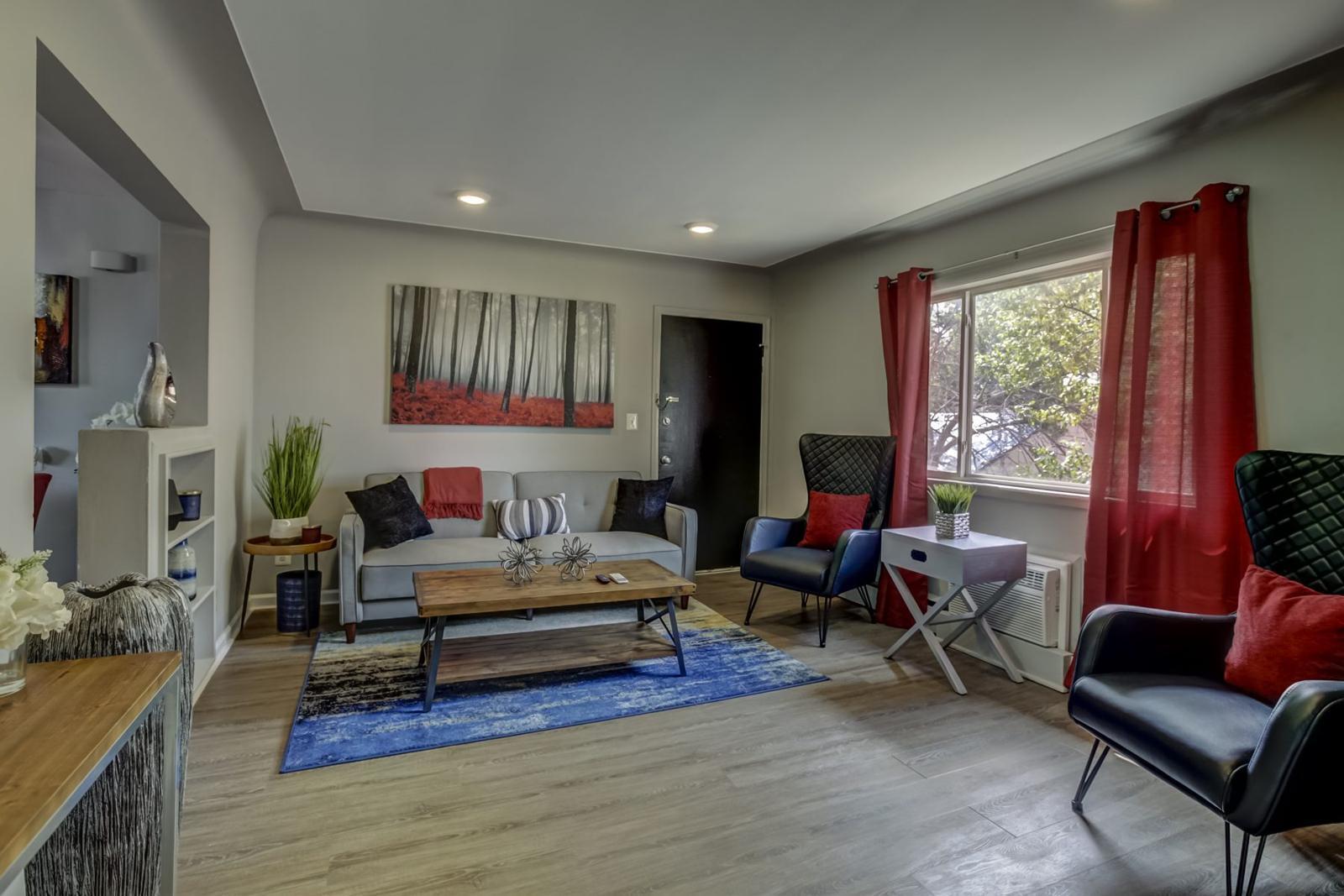 Living room with plank flooring, recessed lights, a gray sofa and red curtains