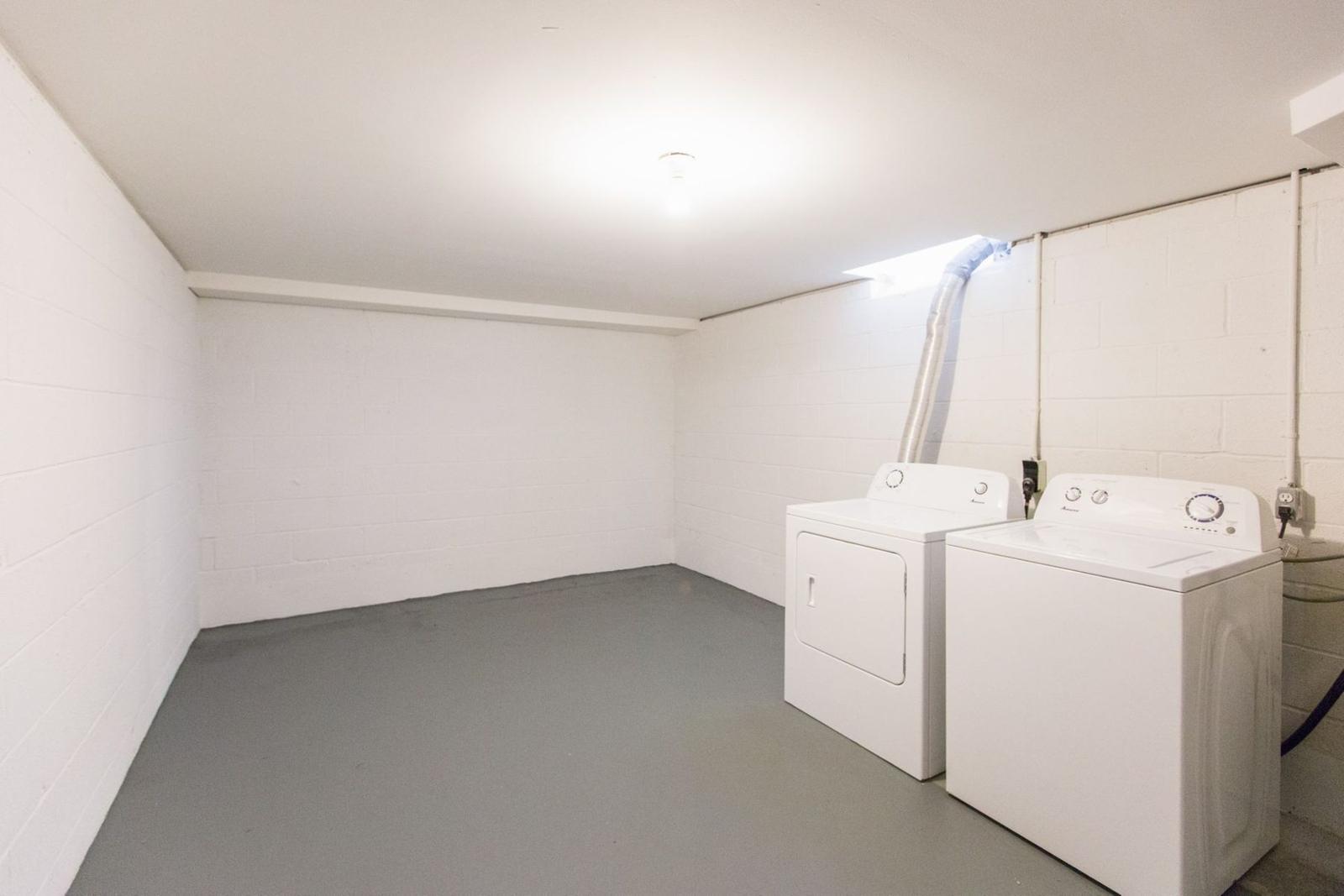 Private 10 by 10 foot laundry and storage room with a washer and dryer, white painted block walls and a gray floor