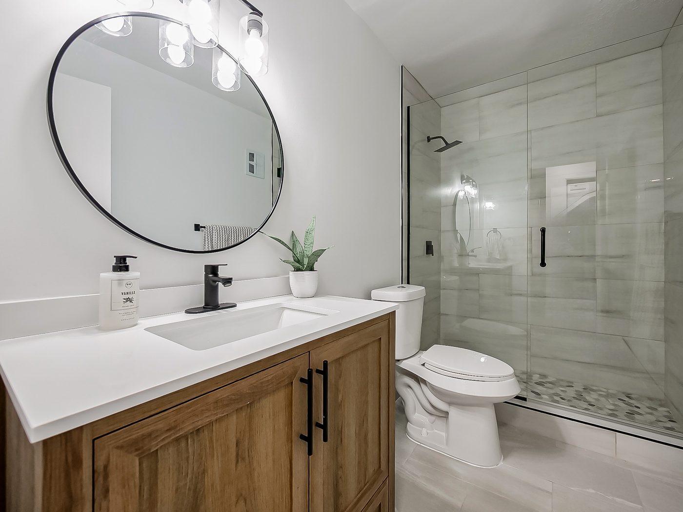 Renovated bathroom with glass-enclosed tile shower and wood vanity
