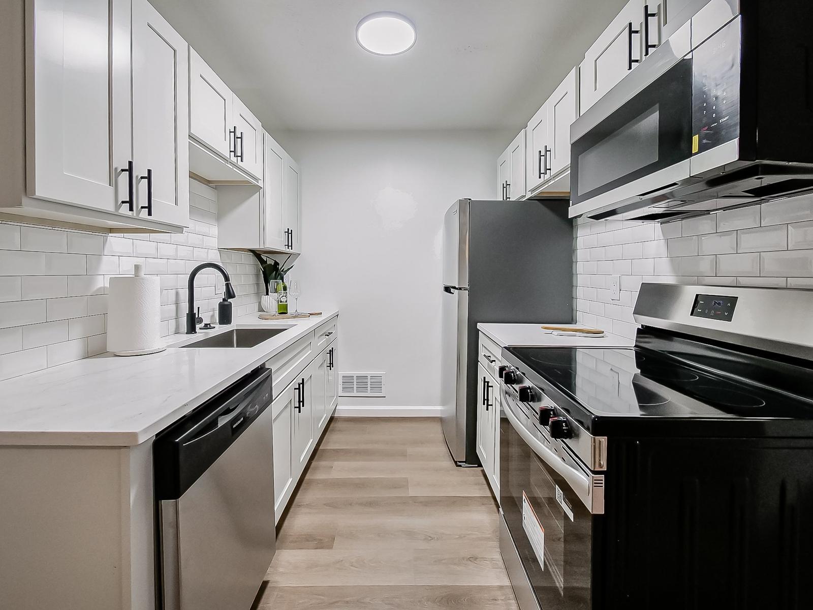Galley kitchen with white shaker cabinets, quartz counters, subway tile and stainless steel appliances