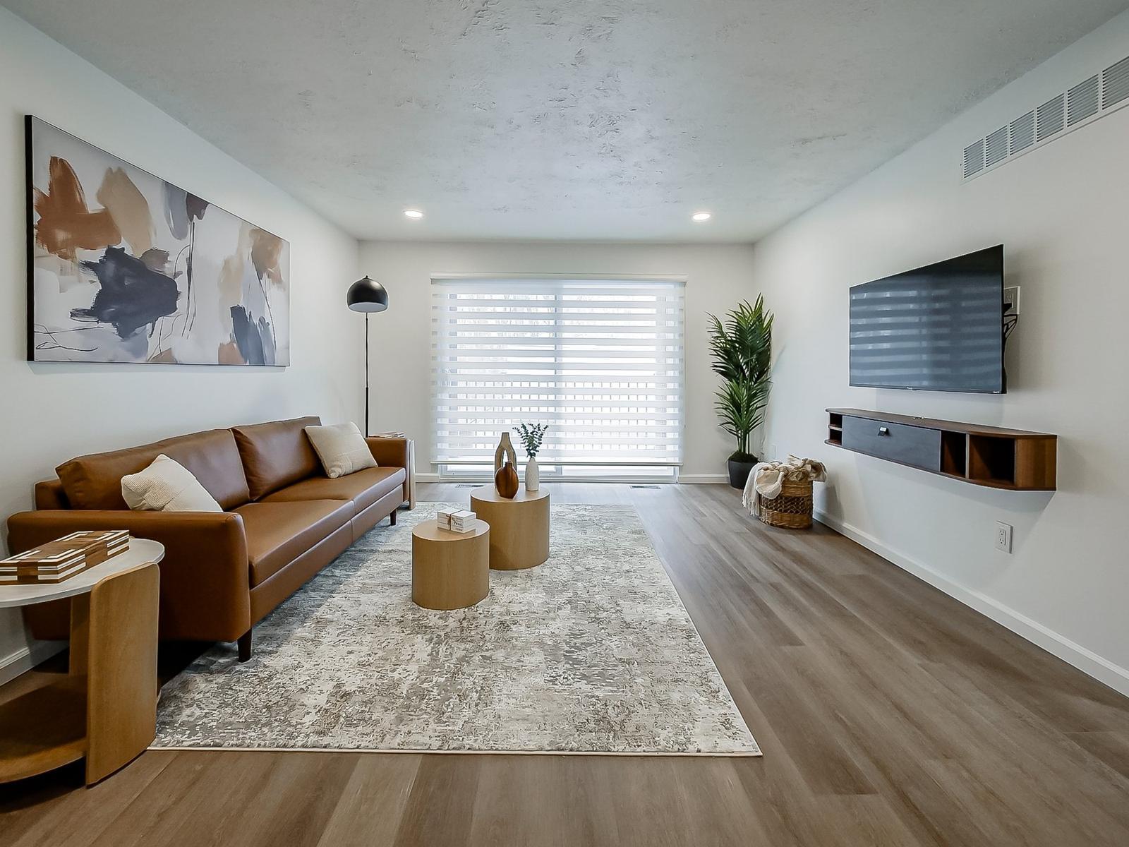 Living room with leather sofa, wall-mounted TV, zebra shades and a doorwall to the private deck