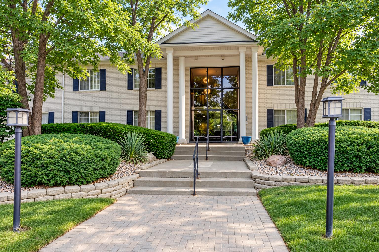 Z on Fourteen cream brick building with a white-columned, two-story glass lobby entrance, navy shutters, mature trees and a paver walkway